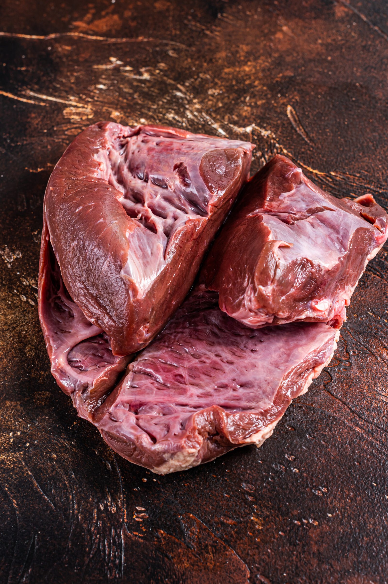 Cut Beef or veal raw heart on a butcher table. Dark background. Top View.