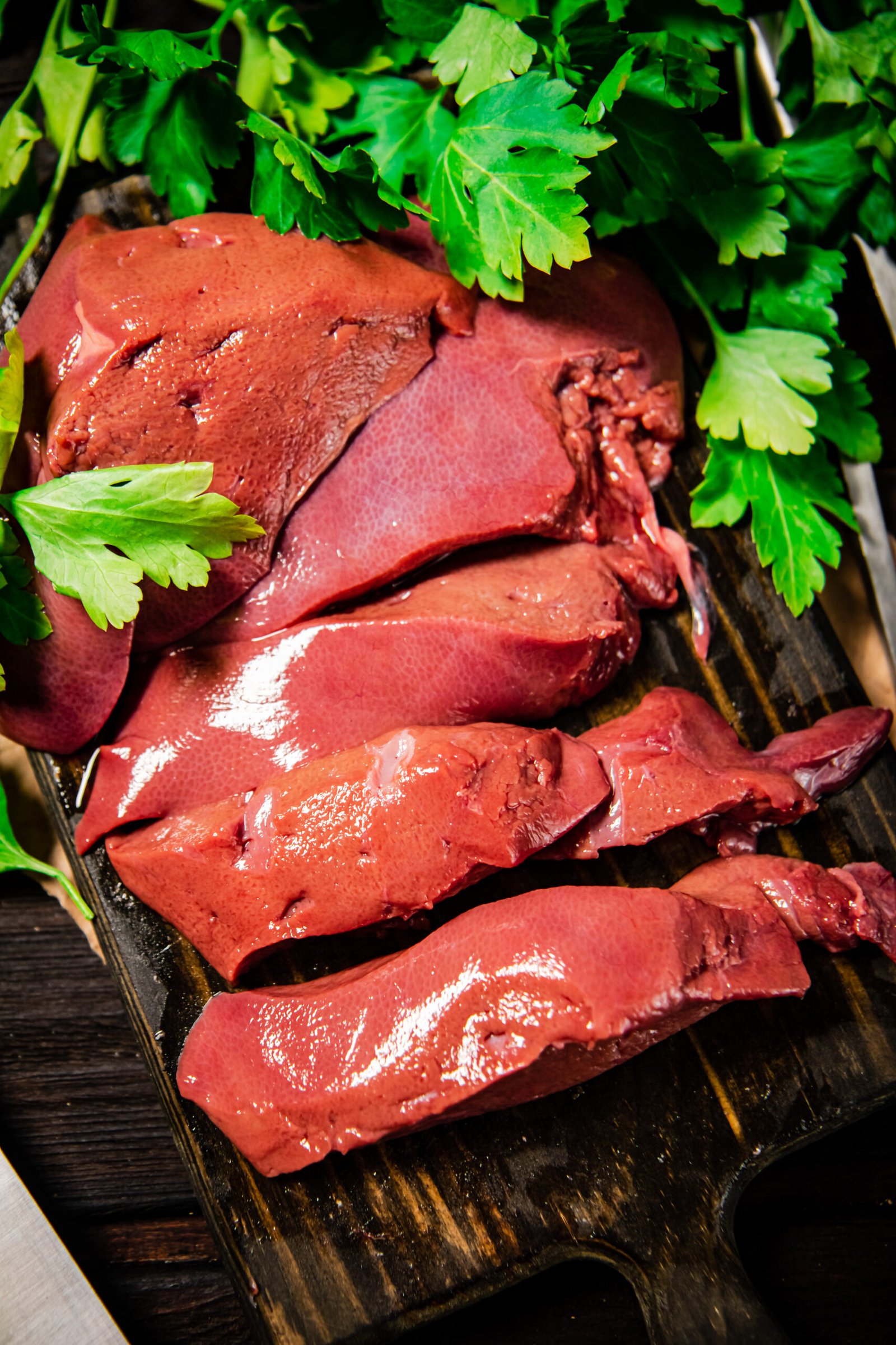 Fresh raw liver on a cutting board with parsley and a knife. On a wooden background. High quality photo