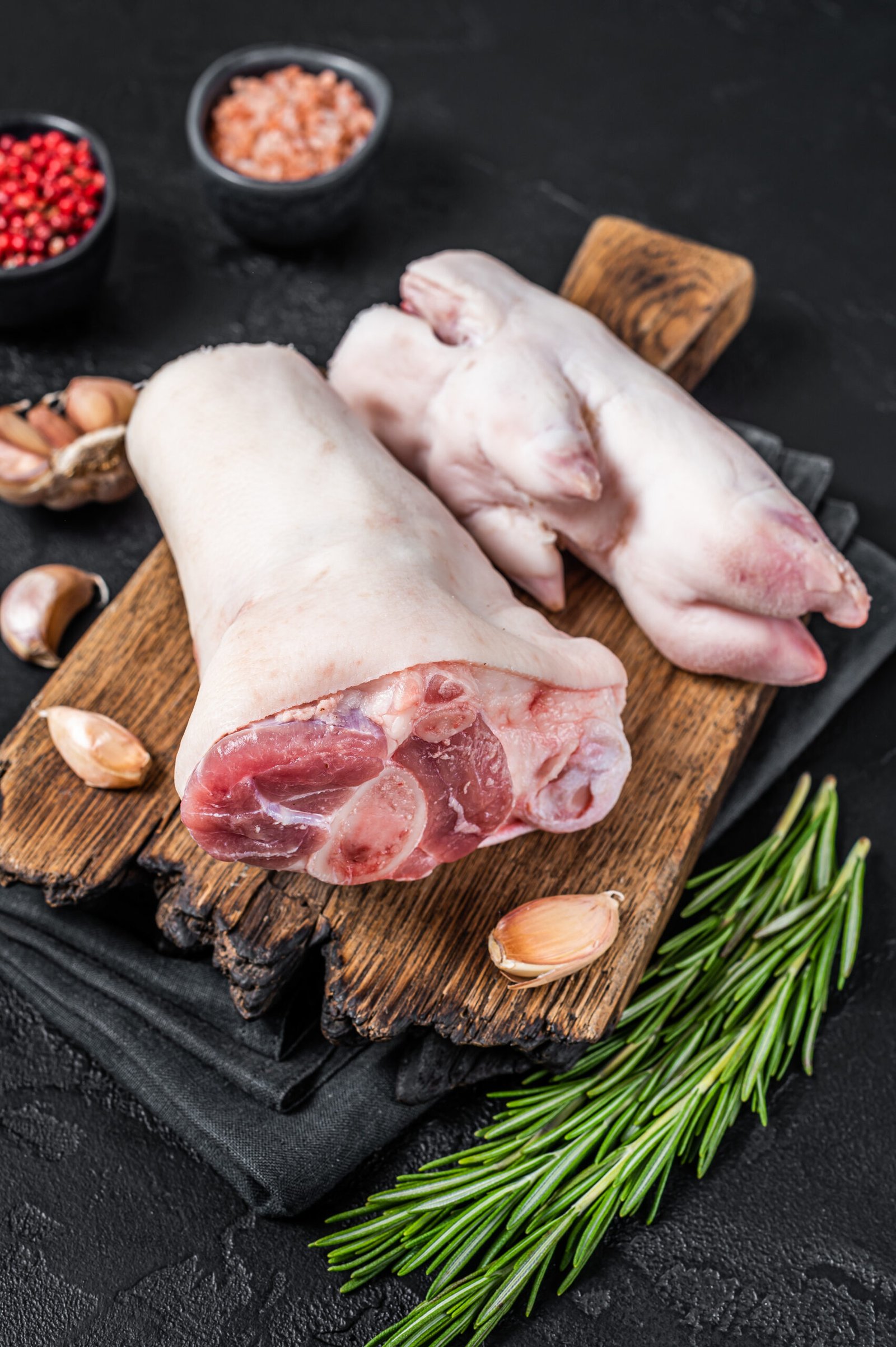 Raw pork knuckle or hoof,  feet on a cutting board. Black background. Top view.